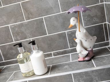 A bathroom shelf with two bottles of bath products and a decorative duck statue holding an umbrella at Gatesgarth in Coniston