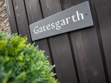 A sign with the word Gatesgarth on a wooden wall with green plants in the foreground at Gatesgarth Coniston