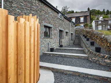 An outdoor area with stone walls and steps next to a stone building with windows and a wooden fence at Gatesgarth in Coniston