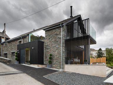 A stone house with black wooden extensions and glass balcony at Gatesgarth in Coniston