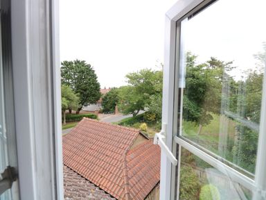 A view through an open window showing a tiled roof and trees outside at Beckhythe Cottage in Overstrand
