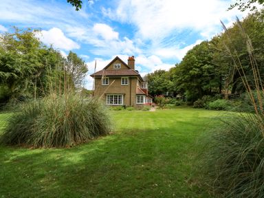 A house with a tiled roof surrounded by grass and trees at Beckhythe Cottage in Overstrand