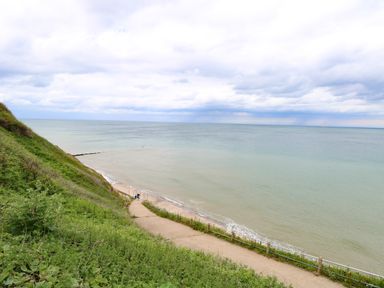 A coastal path leading down to a beach with a grassy hillside on the side at Beckhythe Cottage in Overstrand