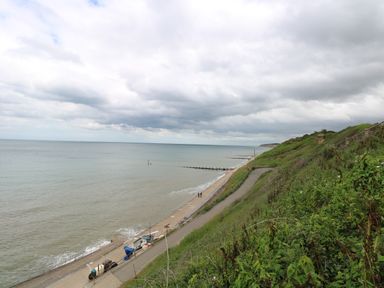 A coastal pathway running along a sea with a sandy beach and groynes visible at Beckhythe Cottage in Overstrand