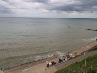 A seafront with a concrete walkway and a small boat on the side at Beckhythe Cottage in Overstrand