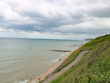 A coastal path along a beach with sea defenses extending into the water and a cloudy sky at Beckhythe Cottage in Overstrand