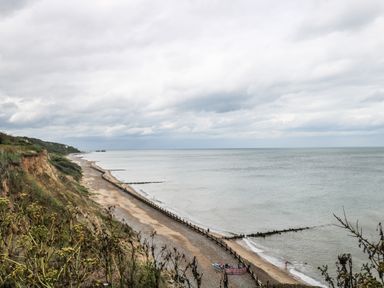 A coastal cliff with vegetation overlooking a beach and sea with groynes at Beckhythe Cottage in Overstrand