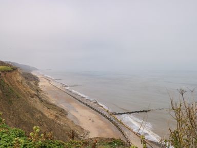 A beach with a cliff and wooden groynes along the shore at Beckhythe Cottage in Overstrand