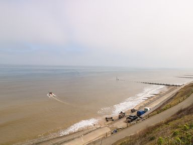 A coastal view with a boat in the sea parked vehicles and wooden groynes along the shoreline at Beckhythe Cottage in Overstrand