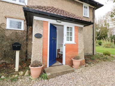 A blue door entrance of a house with two flower pots and a black mailbox at Beckhythe Cottage in Overstrand