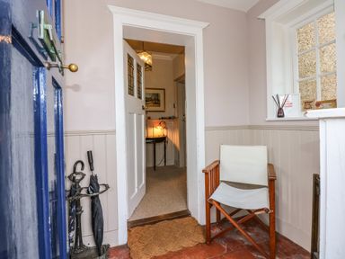 An entryway with a blue door a wooden chair with white fabric an umbrella stand and a doormat at Beckhythe Cottage in Overstrand