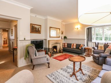 A living room with armchairs a sofa a fireplace and a round wooden table at Beckhythe Cottage in Overstrand