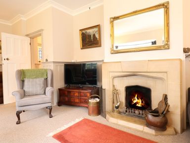 A sitting room with a fireplace a television on a wooden cabinet and an armchair at Beckhythe Cottage in Overstrand