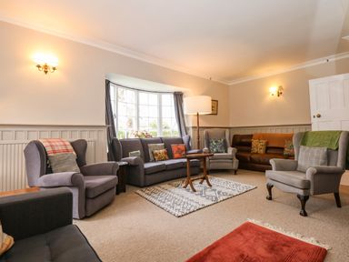 A living room with multiple armchairs sofas and a small round wooden table at Beckhythe Cottage in Overstrand