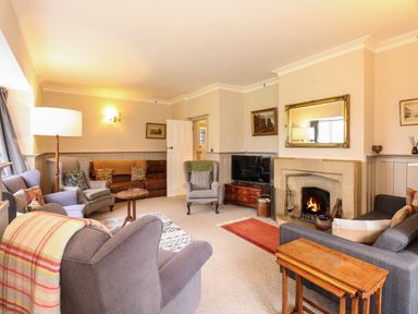 A living room with armchairs sofas a fireplace a television and wooden tables at Beckhythe Cottage in Overstrand