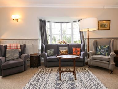 A sitting room with two armchairs sofa table rug and large window at Beckhythe Cottage in Overstrand