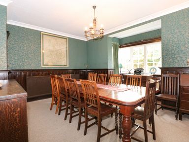 A dining room with a large wooden table surrounded by chairs and a window at Beckhythe Cottage in Overstrand