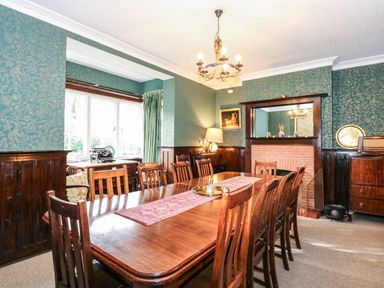 A dining room with a wooden table and chairs a fireplace and a window with green curtains at Beckhythe Cottage in Overstrand