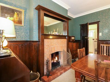 A dining room with a wooden table and chairs and a brick fireplace with a mirror above at Beckhythe Cottage in Overstrand