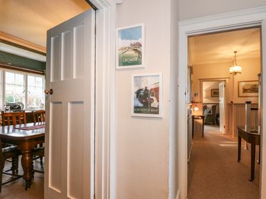 A hallway with framed railway posters on the wall and doors leading to a dining room and a sitting room at Beckhythe Cottage in Overstrand