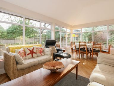 A living room with wicker sofa with cushions and a wooden dining table with chairs at Beckhythe Cottage in Overstrand