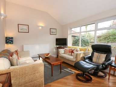 A living room with two sofas a coffee table a TV and a black armchair at Beckhythe Cottage in Overstrand