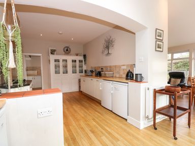 A kitchen with wooden floor cupboards white glass cabinets and small appliances at Beckhythe Cottage in Overstrand
