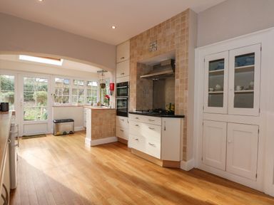 A kitchen with wooden floor cabinets a tiled stove area and glass door cupboard at Beckhythe Cottage in Overstrand