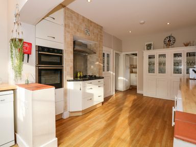 A kitchen with built-in ovens, gas stove, glass-front cabinets, wooden floor, and hanging plant at Beckhythe Cottage in Overstrand