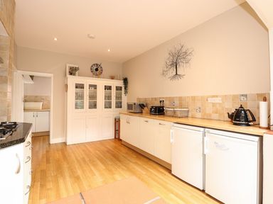 A kitchen with wooden floor white cabinets two small fridges and a glass cabinet at Beckhythe Cottage in Overstrand