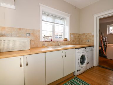 A utility room with a washing machine dishwasher sink cabinets and a window at Beckhythe Cottage in Overstrand
