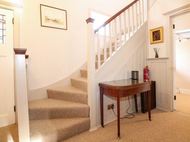 A carpeted staircase with a wooden side table under the stairs a fire extinguisher and framed pictures in a hallway at Beckhythe Cottage in Overstrand