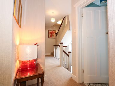 A hallway with a staircase and a wooden side table with a red lamp at Beckhythe Cottage in Overstrand