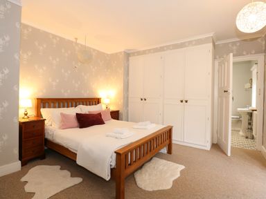 A bedroom with a wooden bed linen on the bed bedside tables and white built in wardrobes at Beckhythe Cottage in Overstrand