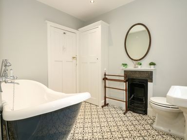 A bathroom with a freestanding bathtub toilet sink mirror and patterned floor at Beckhythe Cottage in Overstrand