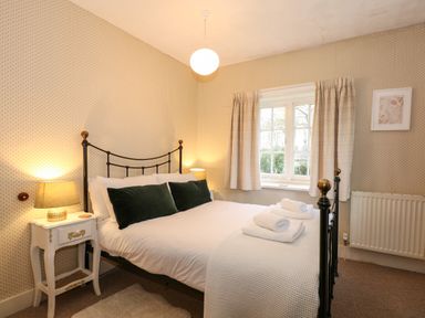 A bedroom with a double bed black metal frame bedside tables with lamps a window with curtains and folded towels on the bed at Beckhythe Cottage in Overstrand