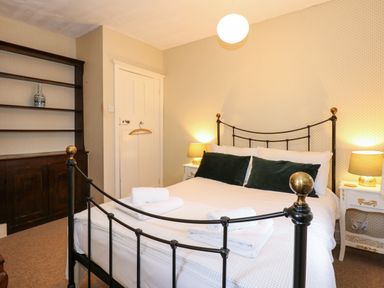 A bedroom with a metal bed frame two bedside tables with lamps and a wooden shelving unit at Beckhythe Cottage in Overstrand