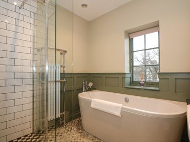 A bathroom with a freestanding bathtub next to a window and a glass-enclosed shower with white subway tiles at Beckhythe Cottage in Overstrand