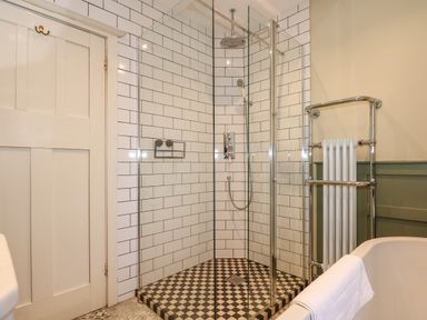A bathroom with a glass enclosed shower with checkered tiles and a towel radiator at Beckhythe Cottage in Overstrand