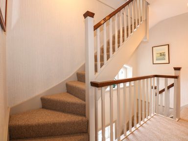 A carpeted staircase with white railings and wooden handrails in a hallway with a framed picture on the wall at Beckhythe Cottage in Overstrand