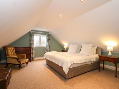A bedroom with a bed bedside tables lamps an armchair a chest of drawers and a window with curtains at Beckhythe Cottage in Overstrand