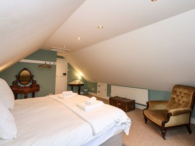A bedroom with a bed towels a vintage armchair a wooden dressing table and a small round table at Beckhythe Cottage in Overstrand