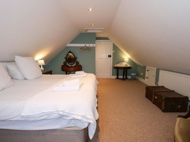 A bedroom with a bed towels on the bed a wooden dresser with mirror a small table with lamp and two trunks on the floor at Beckhythe Cottage in Overstrand