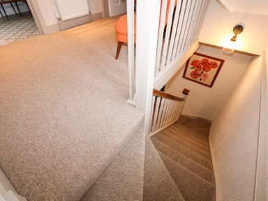 A carpeted staircase with a wooden handrail and a framed flower painting on the wall at Beckhythe Cottage in Overstrand