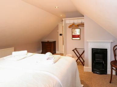 A bedroom with a bed with folded towels a wooden chest of drawers a small fireplace and a chair at Beckhythe Cottage in Overstrand