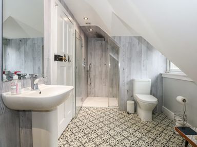 A bathroom with a sink, toilet, shower, patterned floor tiles and light wood paneled walls at Beckhythe Cottage in Overstrand