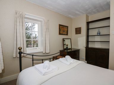 A bedroom with a bed with rolled towels a window curtains a wooden dresser with a mirror and a wooden shelving unit at Beckhythe Cottage in Overstrand