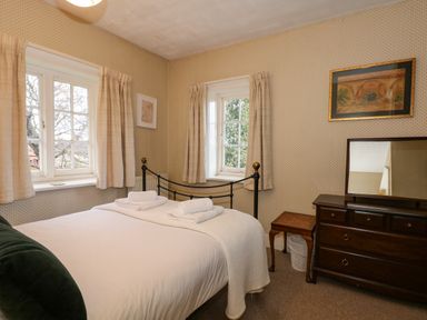 A bedroom with a bed towels dresser mirror and windows at Beckhythe Cottage in Overstrand