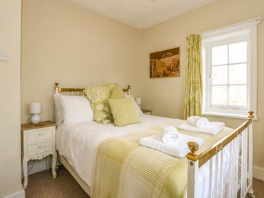 A bedroom with a bed with green and white bedding two bedside tables lamps and a window with green curtains at Beckhythe Cottage in Overstrand