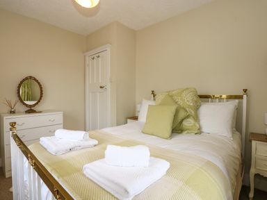 A bedroom with a bed with green and white bedding and pillows two sets of white towels on the bed a white dresser with a round mirror and a door in the background at Beckhythe Cottage in Overstrand